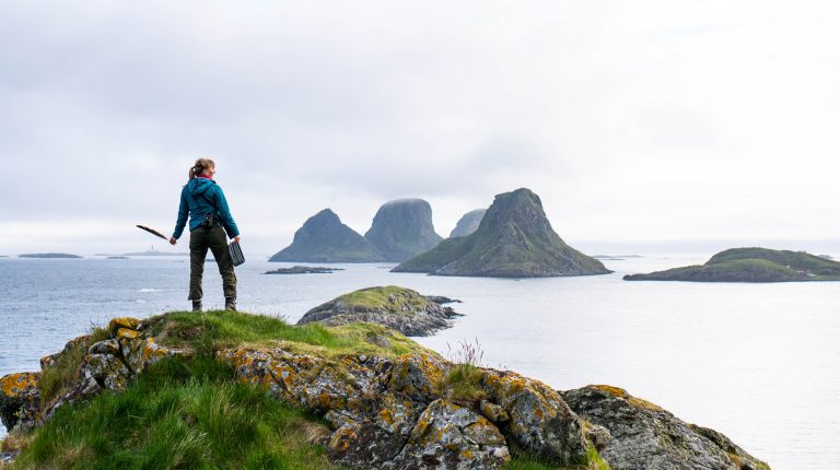 Kvinne med havørnfjær i hånda speider mot Lofot-øyer i havet